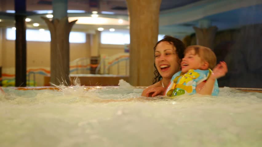 Woman and two children wearing life-jackets bathe in a jacuzzi in a large indoor water park 
