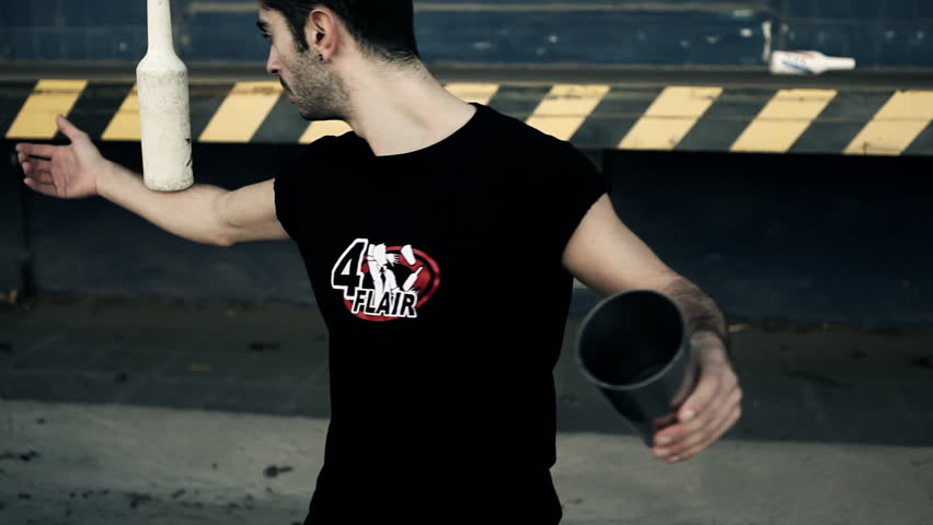 Young man doing flair bar-tending moves in an artistic way with bottle and cup in front of an industrial environment / HD1080 / 29.97 fps