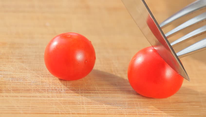 Cherry tomatoes cut with kitchen knife and fork on wooden board