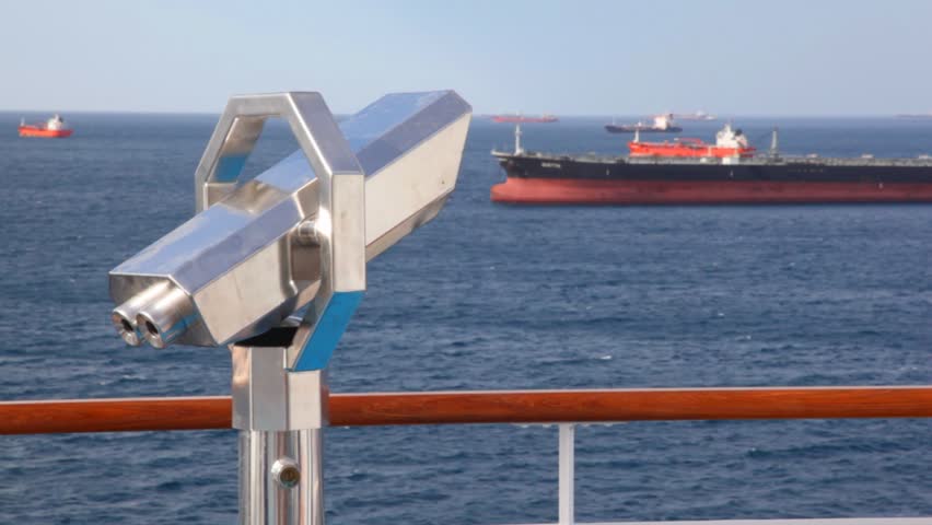 stationary binocular on deck of moving cruise ship in sea near barges