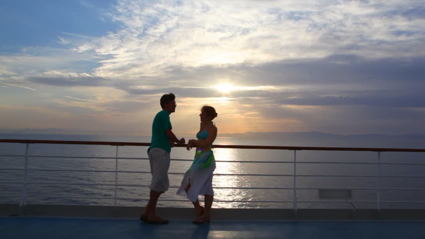 couple having joined hands stands on ship moving in sea during sunset