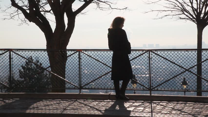 back view of woman standing near the railing on Montmartre hill and looking at Paris