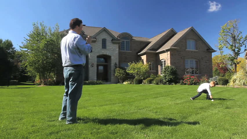 A father and young son play catch in front of their luxury home 