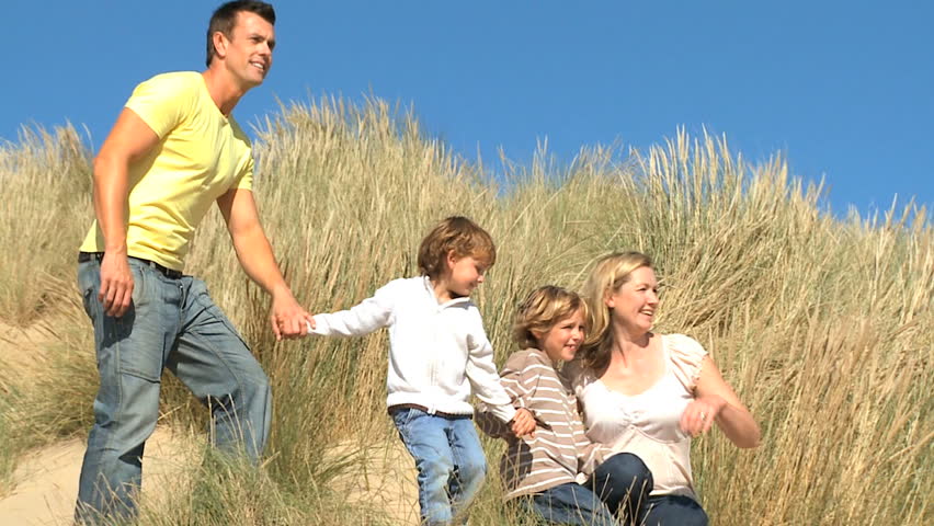 Attractive young caucasian family enjoying outdoor time together on coastal sand dunes  filmed at 60FPS