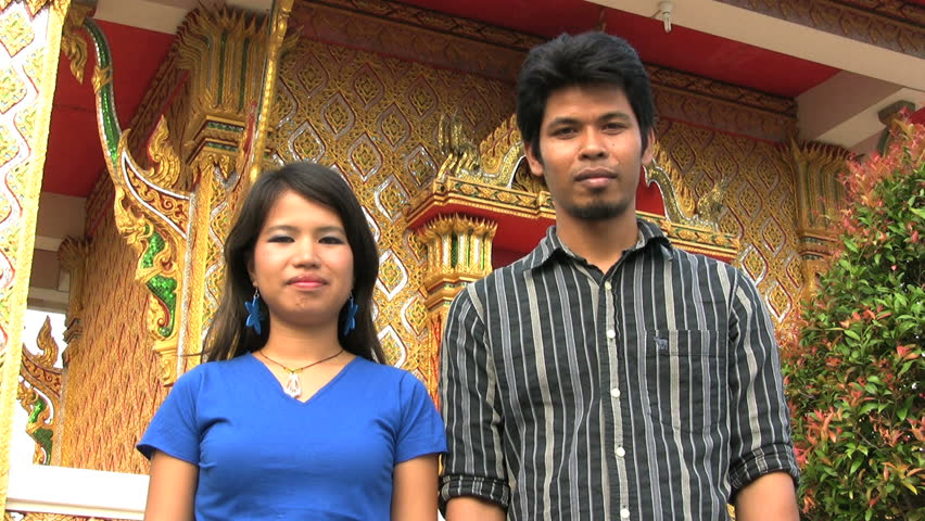 An attractive Thai man and woman demonstrate the typical Thai "wai" greeting outside a Buddhist temple in Bangkok, Thailand.