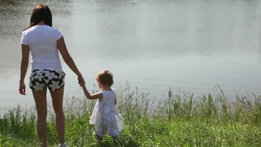 behind mother and her daughter are standing on bank of river 