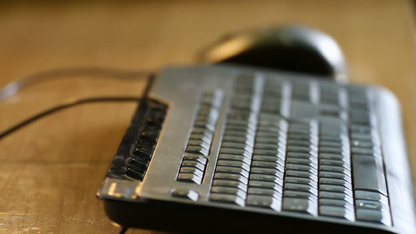 Typing and moving mouse closeup with shallow depth of field over a wood table