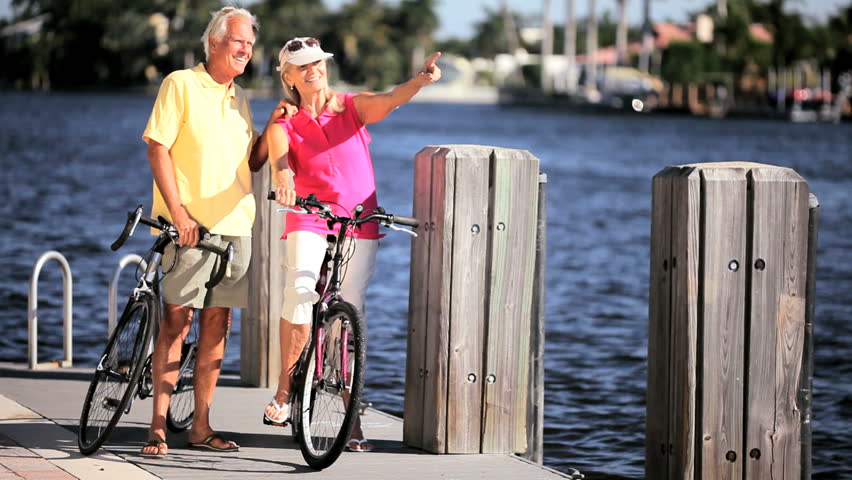Fit & healthy senior couple enjoying each others company while cycling beside a waterway