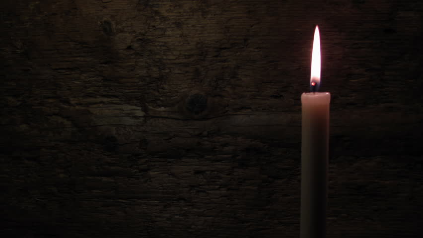 Candle on a wooden background. Fire deflected from the draft.