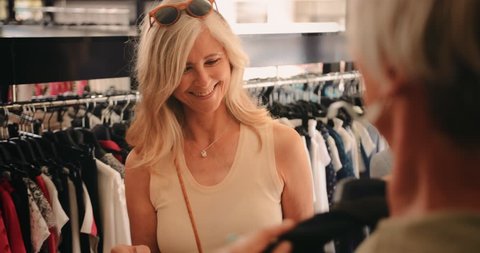 Happy fashionable mature women having fun shopping for clothes in shopping mall clothes store