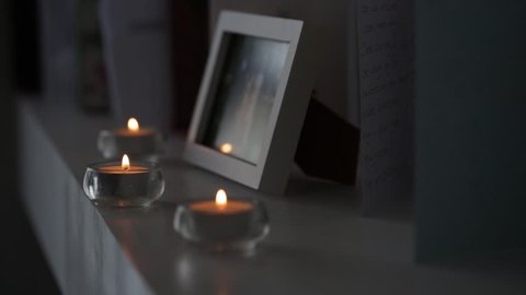 Three Lit Tealight Candles Sit On A While Shelf Next To A Picutre Frame The Flames Flicker And Dance As A Breeze Blows Past Them
