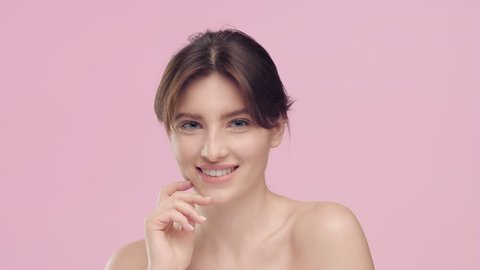 Close-up beauty portrait of young pretty brunette caucasian woman with  smooth healthy skin and nude make-up strokes her smooth skin with pleasure,  looks at camera and smiles | skincare concept