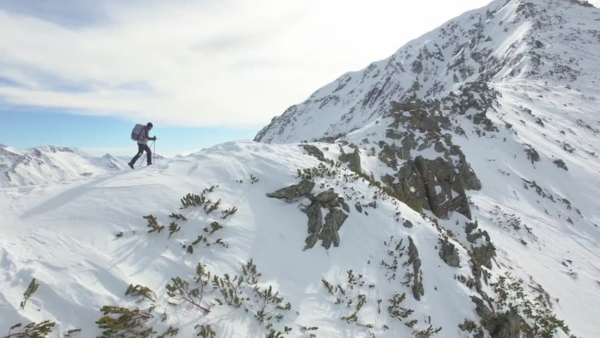 Young Man Walking Up Mountain Slope Backpacking Winter Hike Extreme Conditions Swiss Alps  Aerial Drone Flight Footage 