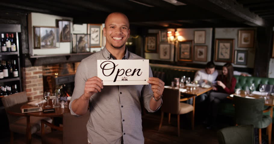 4K Smiling bar owner with new business holds up a sign to show he is now op...