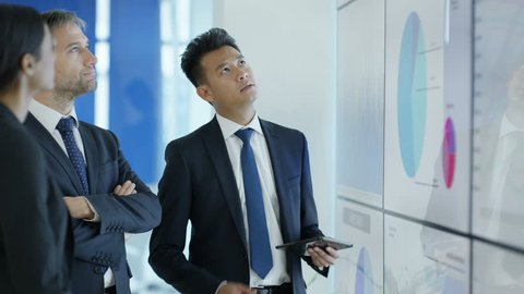 4K Business group in discussion, looking at video screen with charts and graphs (UK-Oct 2016)