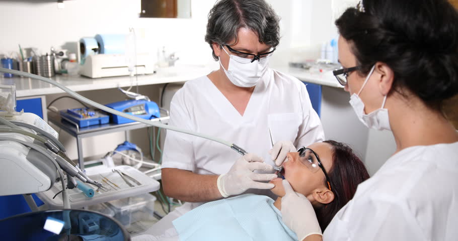 dentist-and-his-dental-nurse-bend-over-their-male-patient-as-he-opens