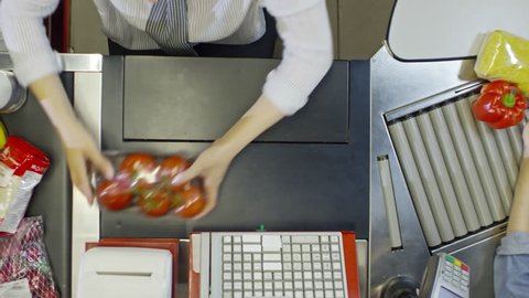 Top view of hands of female cashier scanning groceries at supermarket register in slow motion