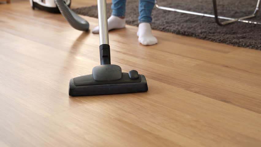Housewife Cleaning Wooden Floor With Vacuum Cleaner In Living Room
