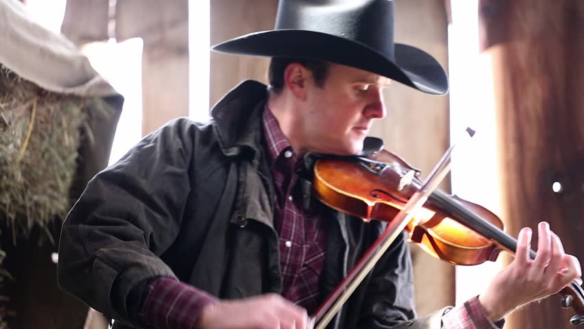 A Cowboy Playing The Fiddle In An Old Barn On Some Haystacks For A